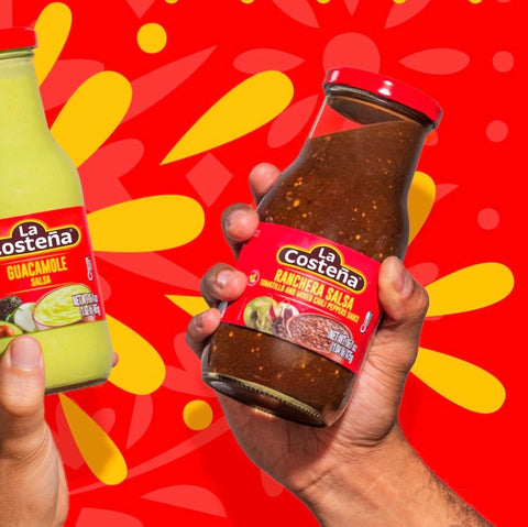 Two hands holding jars of La Costena salsa against a bright red background with yellow abstract shapes. One hand holds a bottle of green guacamole salsa, and the other holds a glass jar of brown ranchera salsa with a red label.