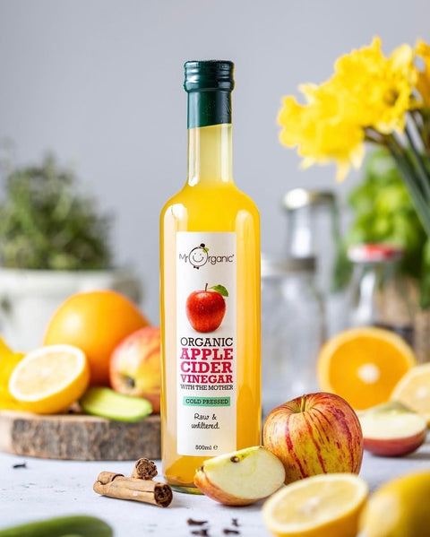 bottle of Mr Organic Apple Cider Vinegar surrounded by apples, oranges, and cinnamon.