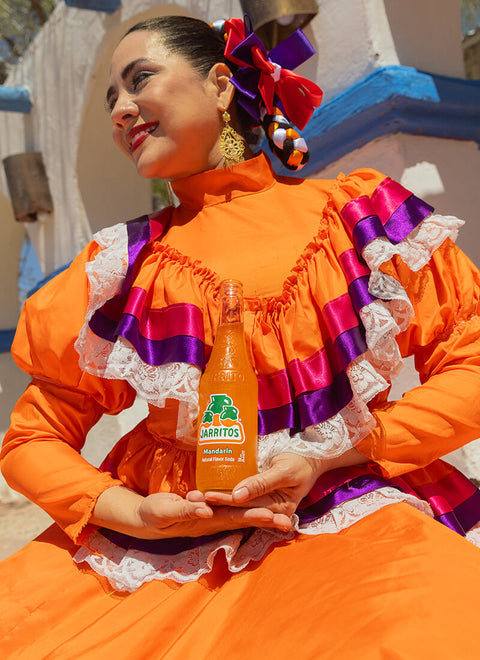 woman in orange dress holding bottle of mandarin jarritos