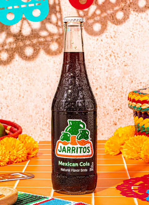 bottle of mexican cola jarritos on an orange surface with decorations in the background