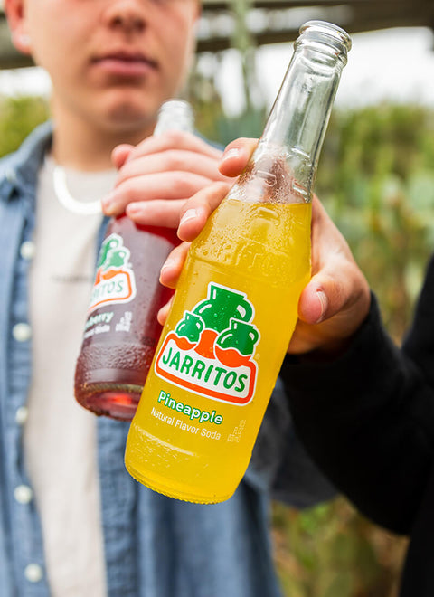 Person holding a Jarritos Pineapple soda bottle outdoors