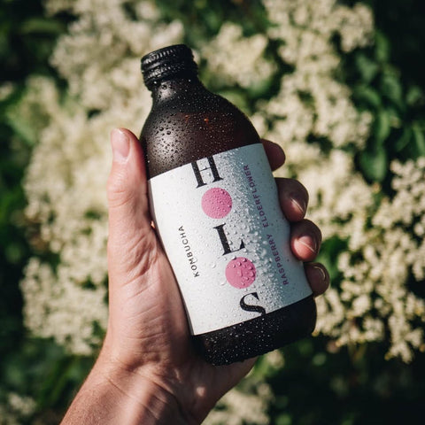 Hand holding raspberry holos in front of elderflowers