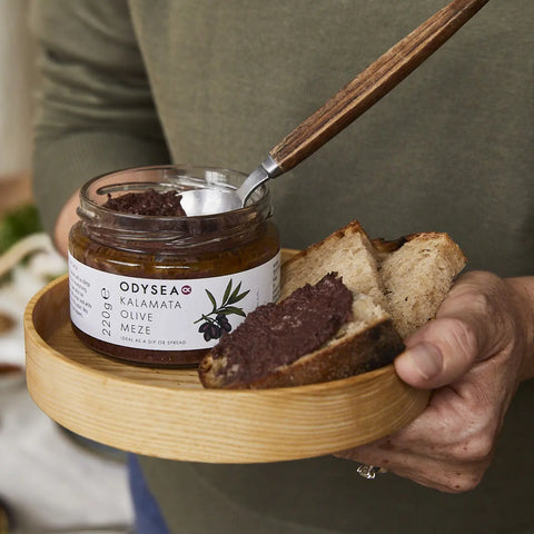 hands holding a wooden board with jar of meze and bread