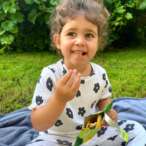Child sitting on grass eating snacks from a bag