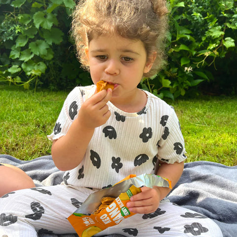 Child eating a snack outdoors on a grassy area
