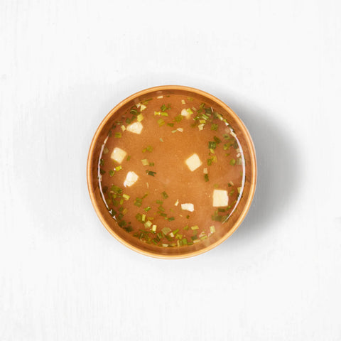 Bowl of soup with green herbs and white cubes on a white background