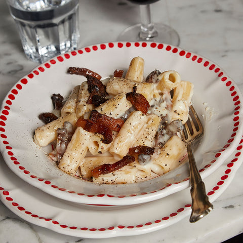 rigatoni pasta dish in white bowl with red dots and a fork