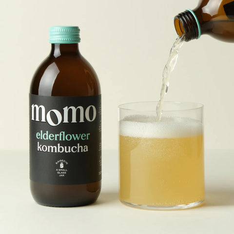 Bottle of momo elderflower kombucha being poured into a glass.