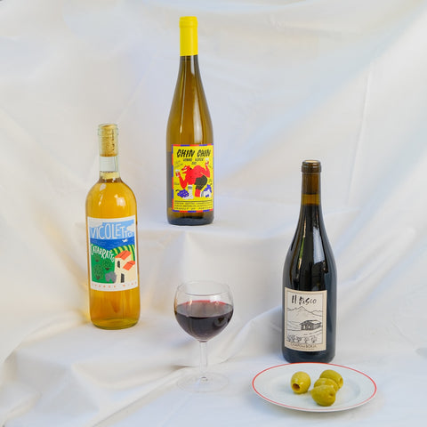 Three natural wine bottles with labels on a white fabric background