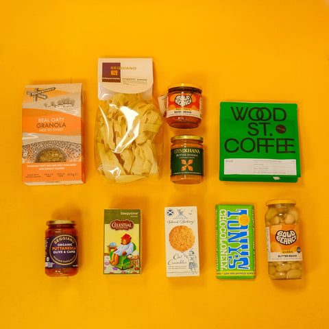 Assorted food products including granola, pasta, coffee, and snacks on a yellow background