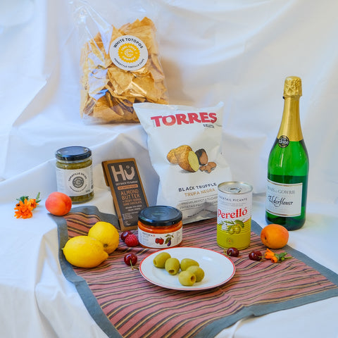 Assorted food items including chips, olives, and a bottle of wine on a table with a white background.