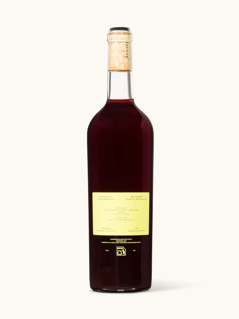 A bottle of red wine with a pale yellow label and a cork stopper, photographed against a solid off-white background.