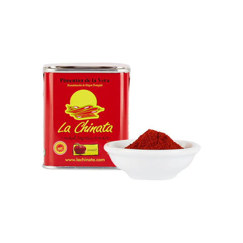 container of la chinata next to small bowl with red powder on a white background