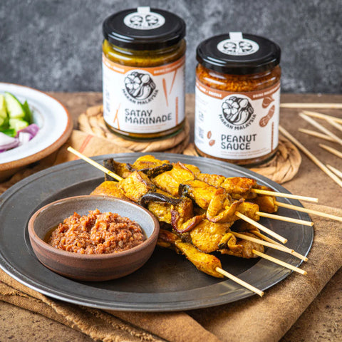 Plated dish with skewered meat and bowl on surface with Makan Malaysia peanut sauce and satay marinade