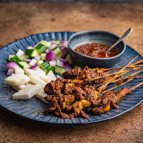 Plated dish with skewered meat, vegetables, and a bowl of sauce on a wooden surface