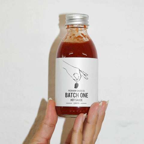 a hand holding up peckham atch one hot sauce bottle