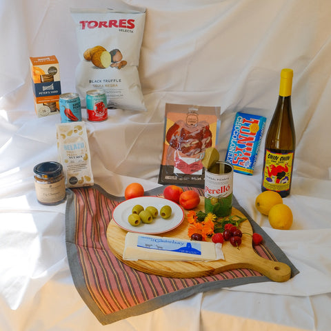 Assorted food items including a bottle of Torres wine, olives, cheese, and fruits on a white background.