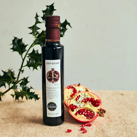 bottle of pomegranate molasses next to pomegranate on brown surface