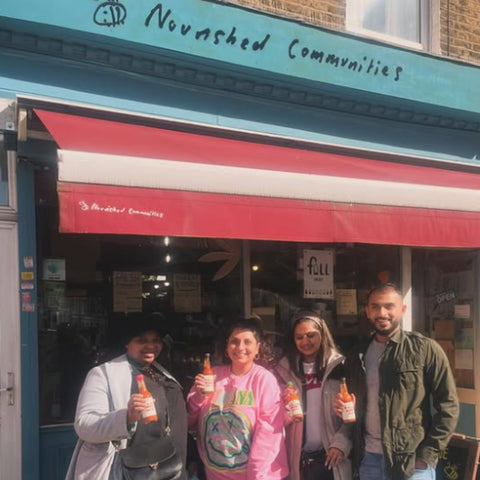 owners of raja bonnet original hot sauce standing outside a building with 'Nourished Communities' sign holding a bottle of raja bonnet original hot sauce