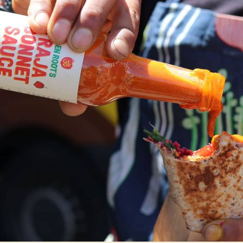 Person pouring Raja Sonnet sauce from a bottle onto a sandwich.