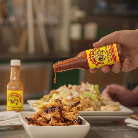 dirty dick's hot sauce bottle with sweet and spicy blend of habanero, mango, banana, and brown sugar. vegan, gluten-free, and all-natural ingredients on top of chicken 