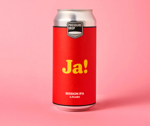 A red aluminum can of Pressure Drop Ja! Session IPA with yellow lettering, set against a solid pink background.