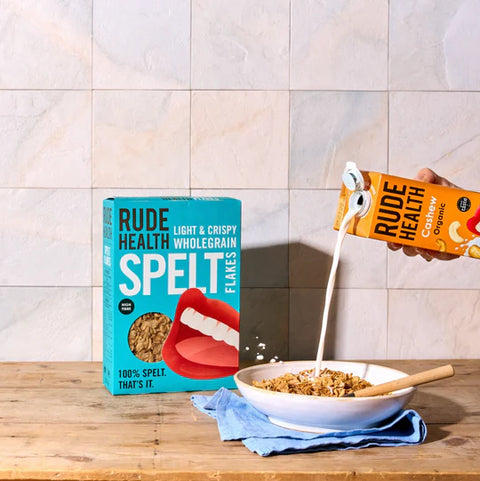 hand pouring rude health cashew organic drink into bowl of cereal on wooden surface