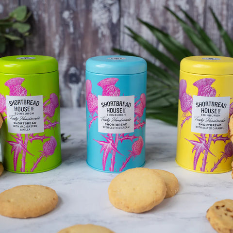 three tins of shortbread side by side with iscuits in front