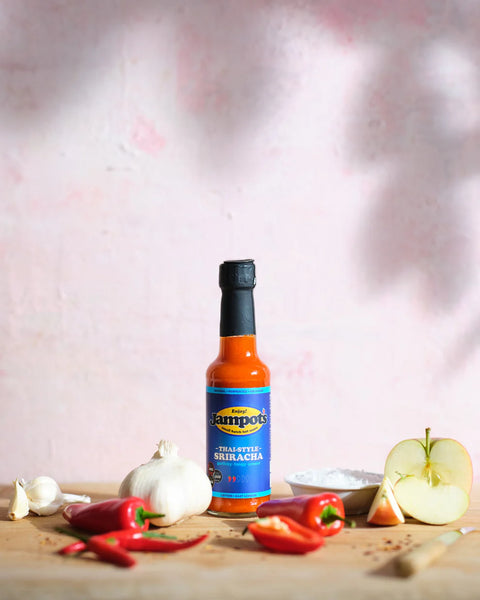 bottle of sauce on a wooden surface surrounded by peppers and onions