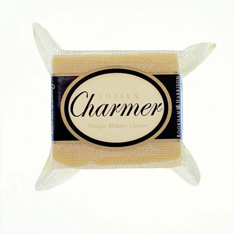 A packaged block of Sussex Charmer Unique Mature Cheese by Bookham & Harrison, wrapped in a textured white paper sleeve with a central oval label in cream, black, and gold.