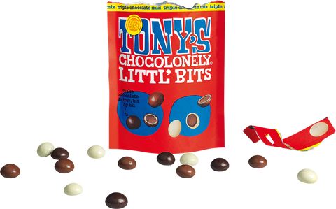 A red bag of Tony's Chocolonely Little Bits chocolate candies stands upright on a white background, with several chocolate pieces scattered around it and a torn piece of the packaging lying to the right.