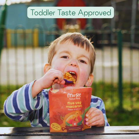Child eating from a box labeled 'Toddler Taste Approved' with a playground in the background