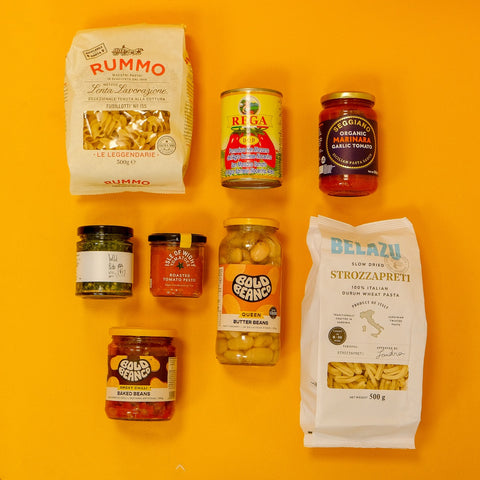 Assorted food products including pasta and canned goods on a bright yellow background