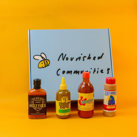 Four hot sauce bottles on a yellow background with 'Nourished Communities' hamper box.