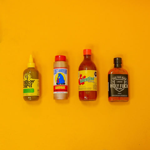 Four hot sauce bottles with colorful labels on a yellow background