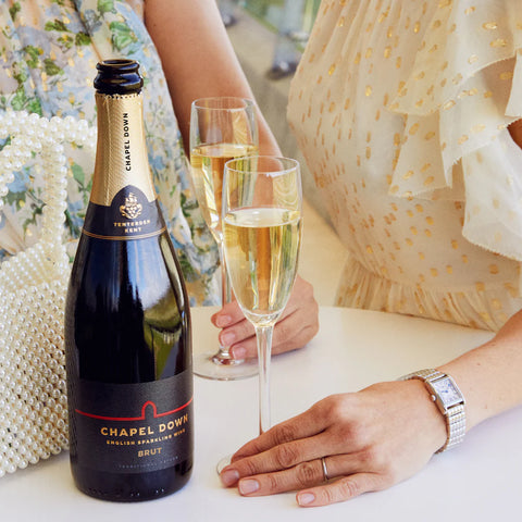 bottle of brut and hands holding filled champagne glasses on surface