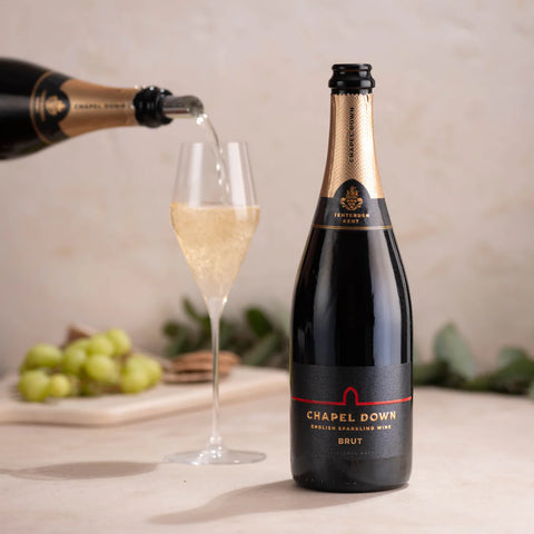Bottle of Chapel Down sparkling wine being poured into a glass with grapes in the background.
