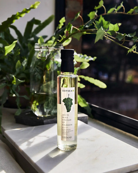 bottle of white wine vinegar of kalamata on white surface in front of plants