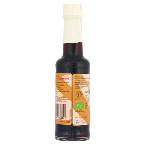 A bottle of organic soy sauce shown from the back, featuring a dark brown liquid, a cream-colored neck seal, and a tan and orange label with text and a green organic certification logo.