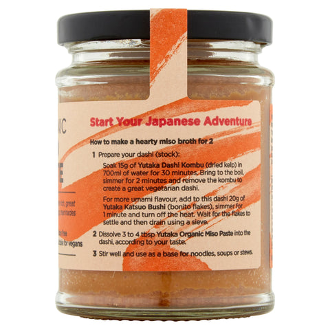 A glass jar of Yutaka  miso paste with a black lid and a beige label featuring orange graphics and recipe text, shown on a white background.
