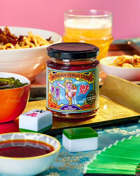 jar of Sichuan Chilli Crisp on surface with bowls of food surrounding 