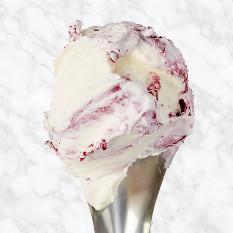 A scoop of creamy white ice cream with red berry swirls served in a metal scoop against a white marble background.