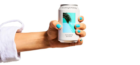 A hand with bright turquoise nail polish holds a slim white can of coconut coconut coffee against a plain white background.