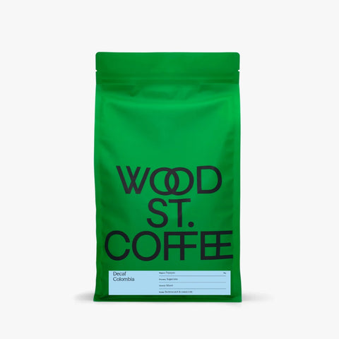 A bright green stand-up coffee bag with large black text reading 'WOOD ST. COFFEE' and a small light blue label near the bottom, shown on a plain light gray background.
