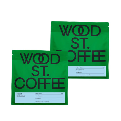 Two green Wood St. Coffee coffee bags with black lettering and white labels, shown on a plain white background.