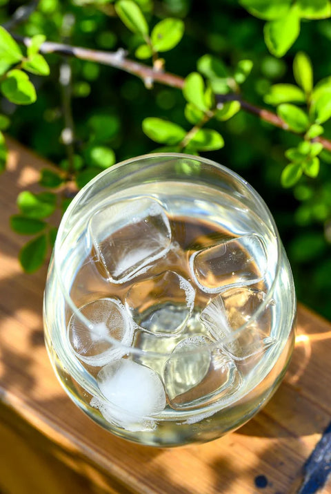 Clear glass with iced drink on a wooden surface with green foliage in the background