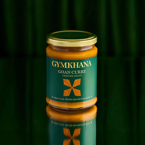 A glass jar of GYMKHANA Goan Curry Cooking Sauce with a gold lid and a dark green label, set against a dark green background with a clear reflection below.