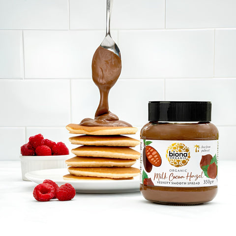 Biona Organic Milk Cacao Hazelnut spread jar with pancakes and raspberries on a white background