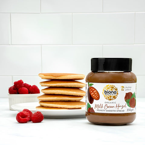 Jar of Biona Organic spread with pancakes and raspberries on a white background