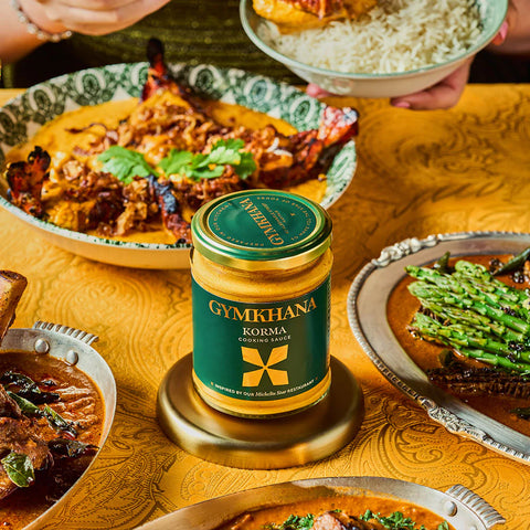 jar of korma cooking sauce on an orange surface surrounded by food dishes